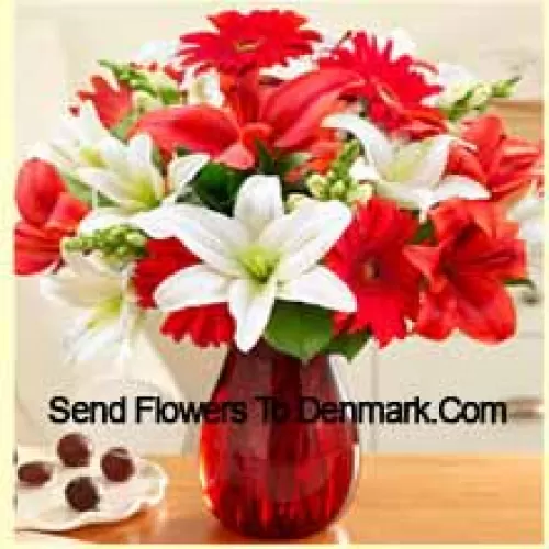Gerberas rouges, lys blancs, lys rouges et autres fleurs assorties disposées magnifiquement dans un vase en verre