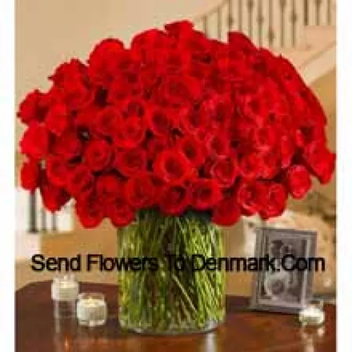 101 roses rouges avec quelques fougères dans un grand vase en verre